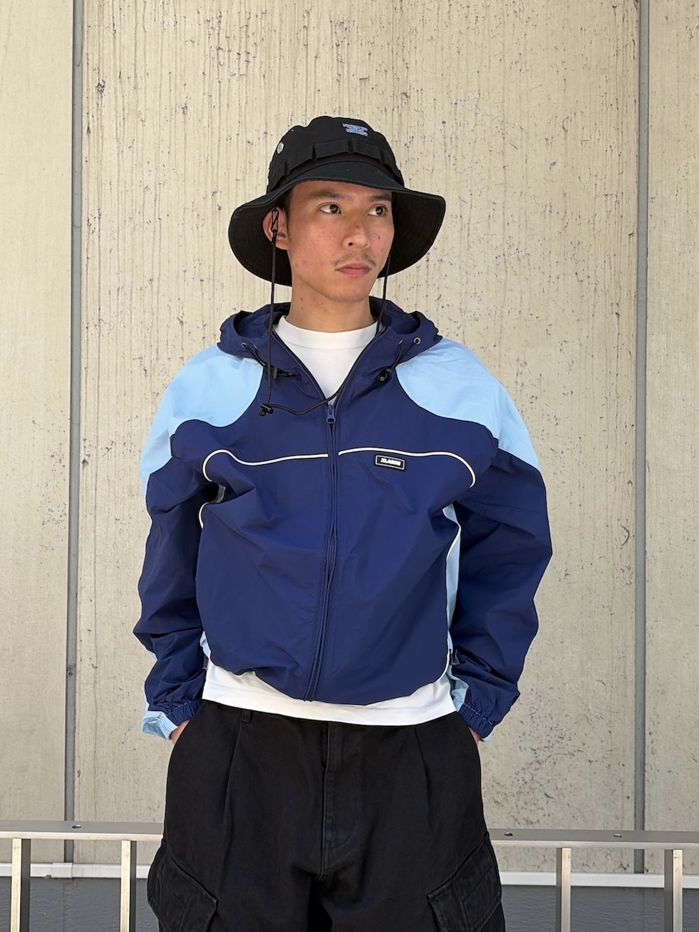 ブルー系のナイロンジャケット、ブラック系のカーゴパンツ、ブラック系のハットを着用したメンズの春コーディネートの5枚目の写真