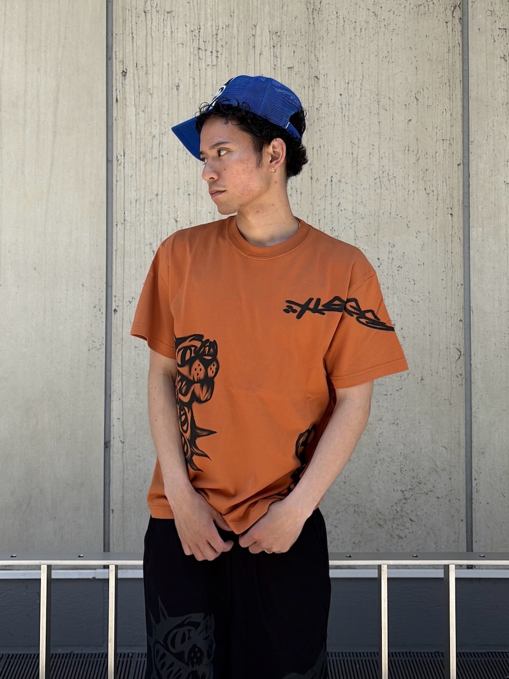 オレンジ系のTシャツ/カットソー、ブラック系のスウェットパンツ、ブルー系のキャップを着用したメンズの春コーディネートの7枚目の写真