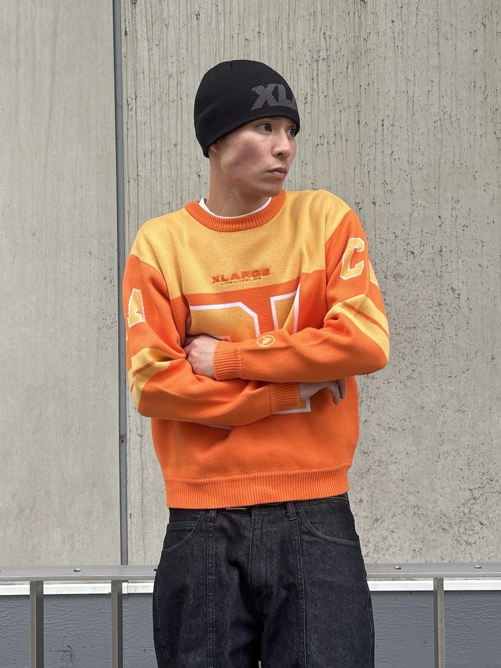 オレンジ系のニット/セーター、ブラック系のデニムパンツ、ピンク系のニットキャップ/ビーニーを着用したメンズの冬コーディネートの5枚目の写真