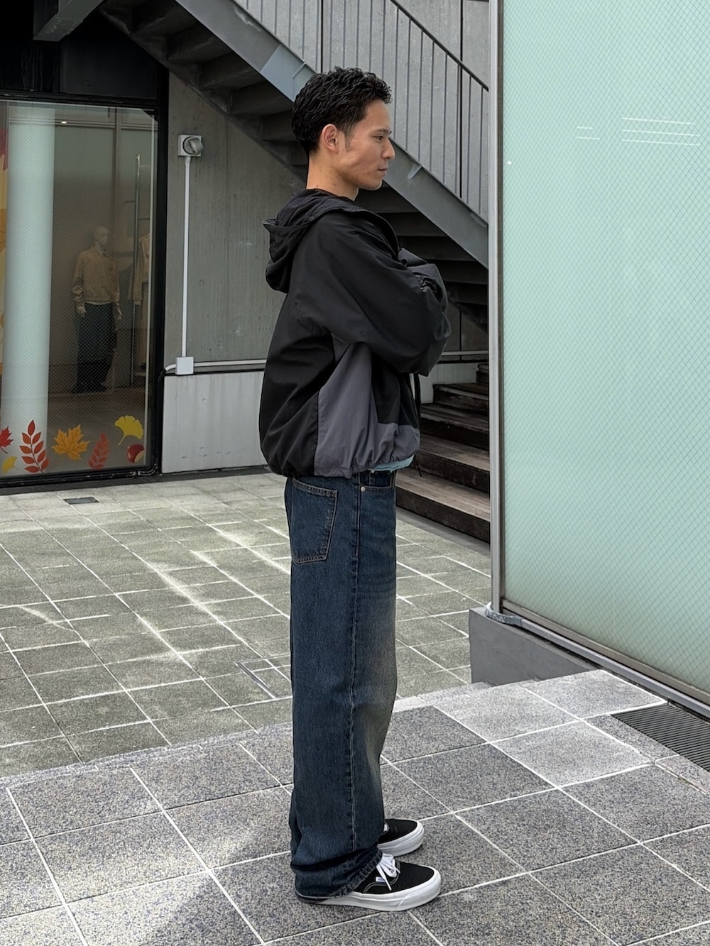 レッド系のナイロンジャケット、グレー系のスウェット、ブルー系のデニムパンツを着用したメンズの秋コーディネートの4枚目の写真