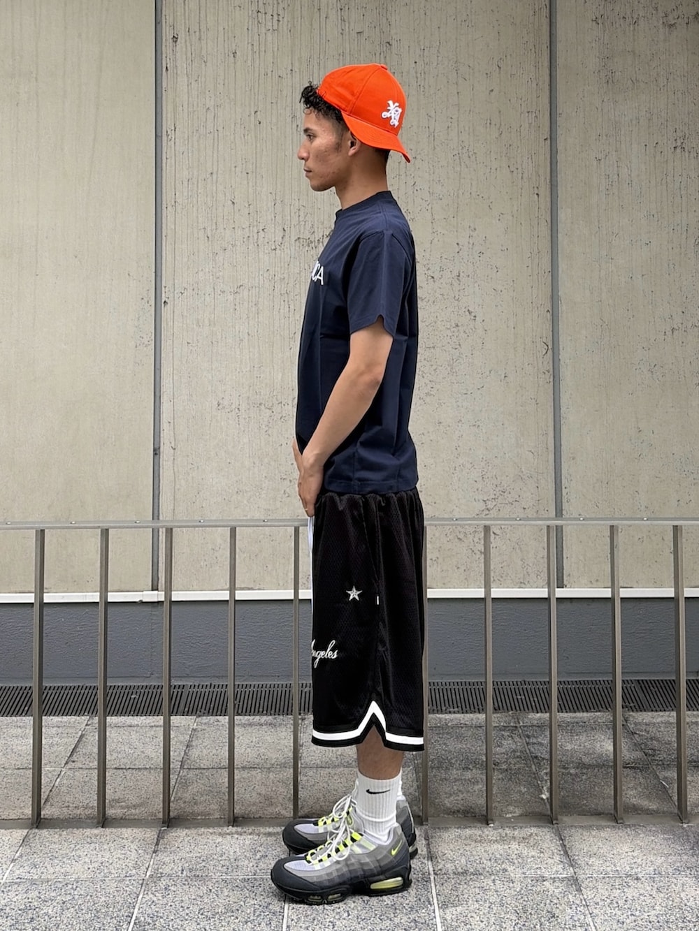 ブラック系のその他パンツ、ブルー系のTシャツ/カットソー、オレンジ系のキャップを着用したメンズの夏コーディネートの3枚目の写真