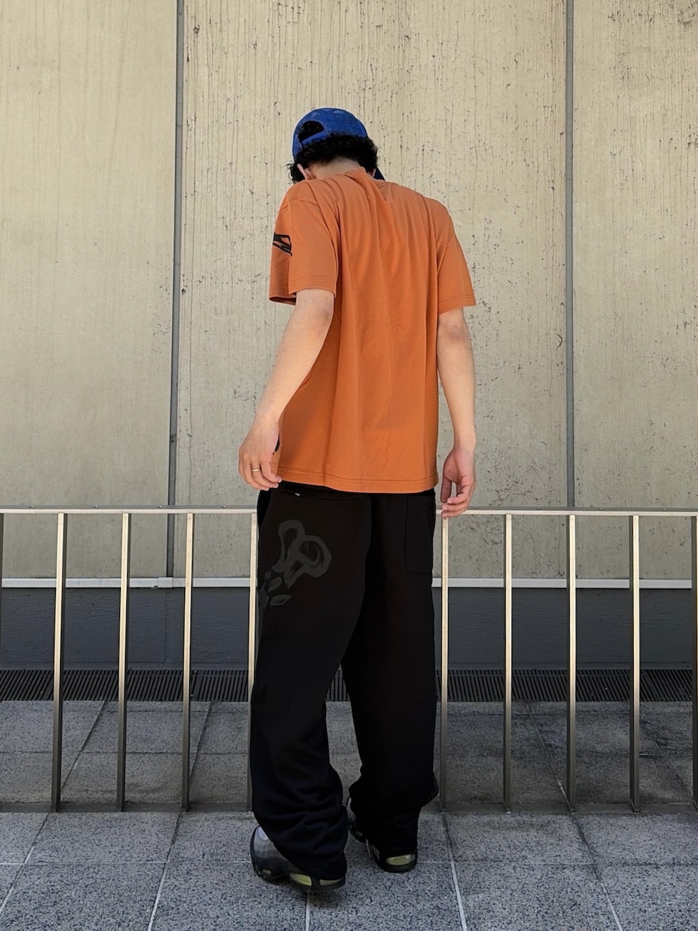 オレンジ系のTシャツ/カットソー、ブラック系のスウェットパンツ、ブルー系のキャップを着用したメンズの春コーディネートの5枚目の写真