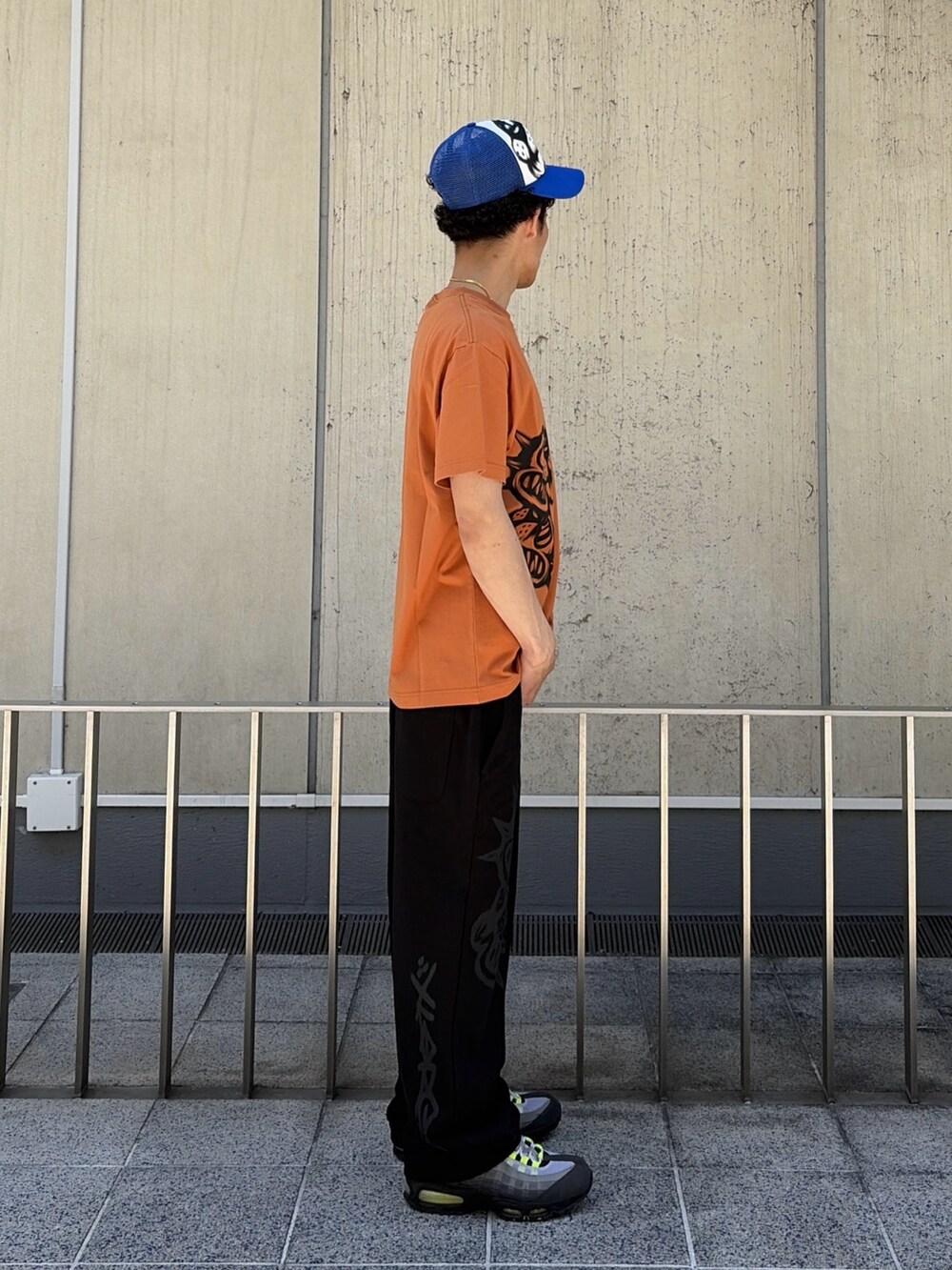 オレンジ系のTシャツ/カットソー、ブラック系のスウェットパンツ、ブルー系のキャップを着用したメンズの春コーディネートの4枚目の写真