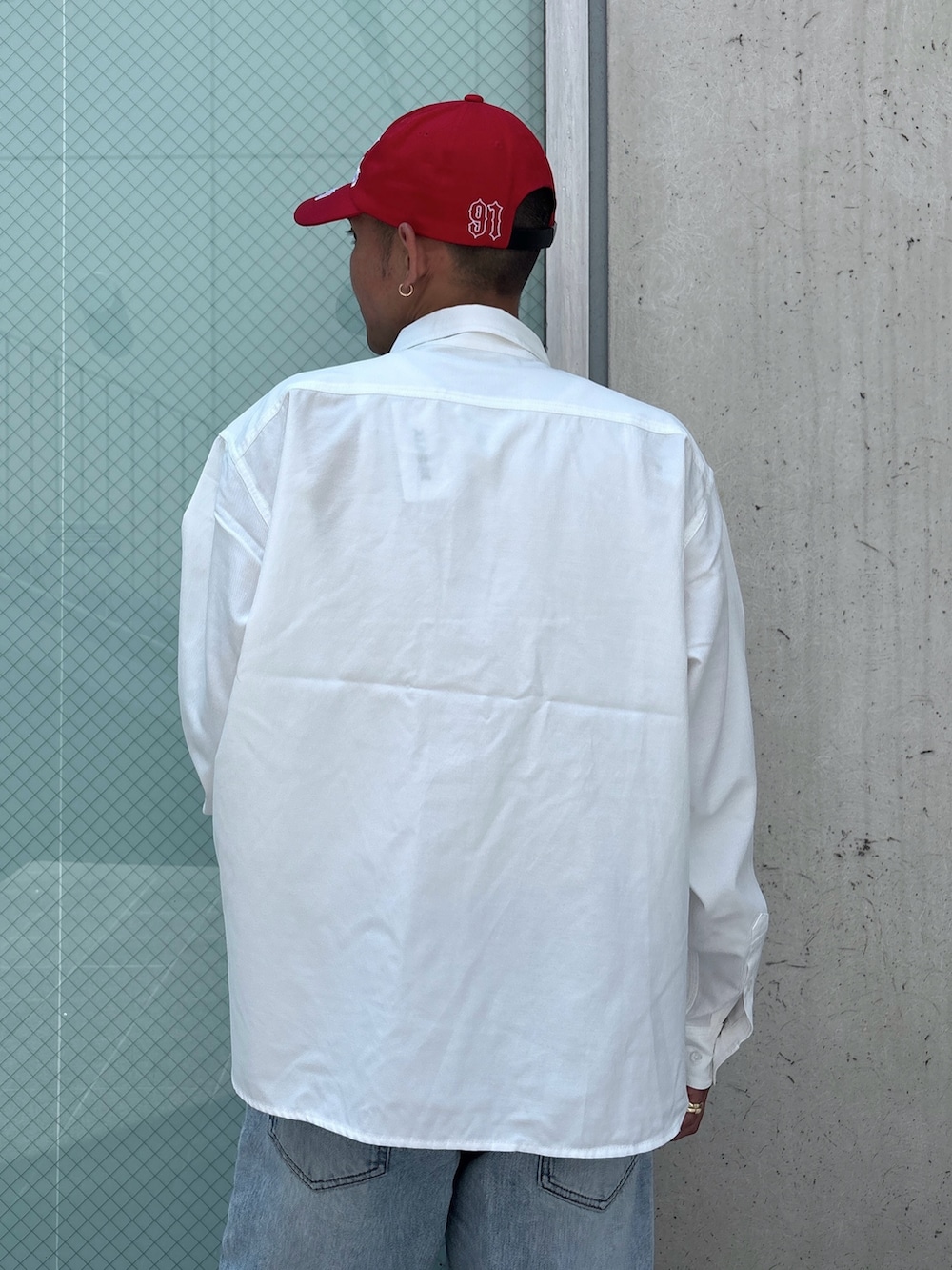 ブルー系のデニムパンツ、ホワイト系のシャツ/ブラウス、レッド系のキャップを着用したメンズの秋コーディネートの6枚目の写真