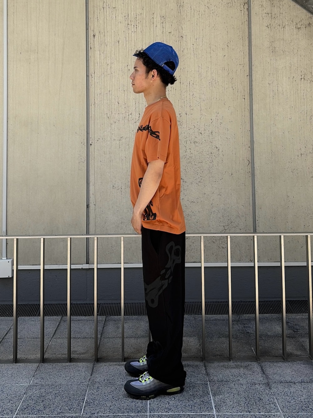 オレンジ系のTシャツ/カットソー、ブラック系のスウェットパンツ、ブルー系のキャップを着用したメンズの春コーディネートの3枚目の写真