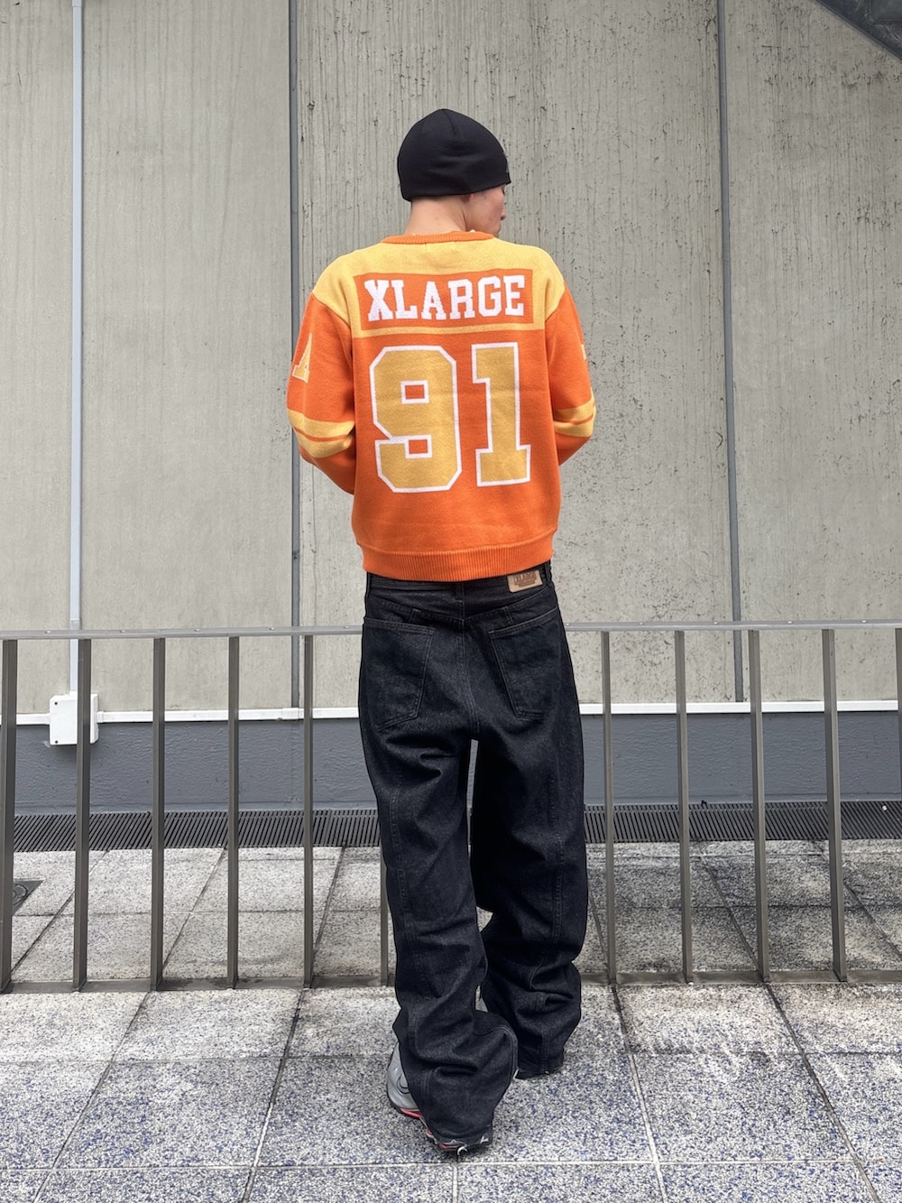 オレンジ系のニット/セーター、ブラック系のデニムパンツ、ピンク系のニットキャップ/ビーニーを着用したメンズの冬コーディネートの4枚目の写真