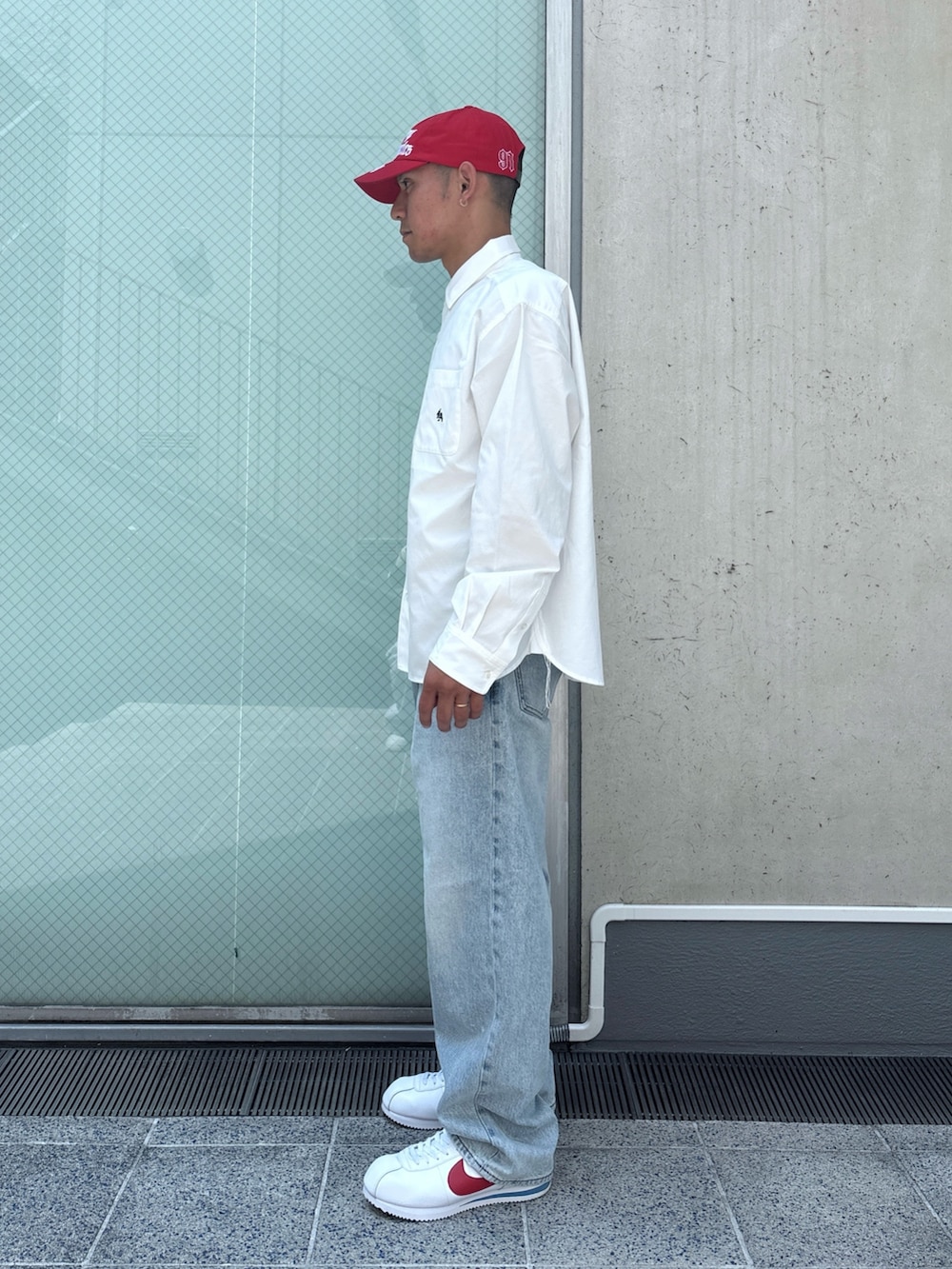 ブルー系のデニムパンツ、ホワイト系のシャツ/ブラウス、レッド系のキャップを着用したメンズの秋コーディネートの2枚目の写真