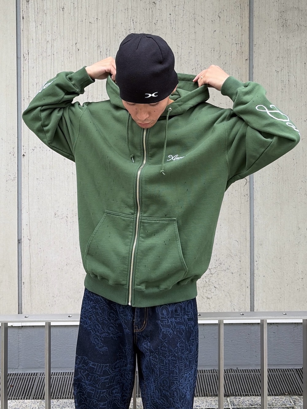 グリーン系のパーカー、ブルー系のデニムパンツ、レッド系のニットキャップ/ビーニーを着用したメンズの秋コーディネートの6枚目の写真