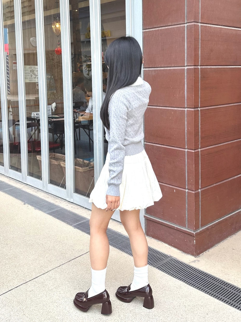 ホワイト系のスカート、グレー系のカーディガン/ボレロ、ブラウン系のローファーを着用したレディースの秋コーディネートの3枚目の写真