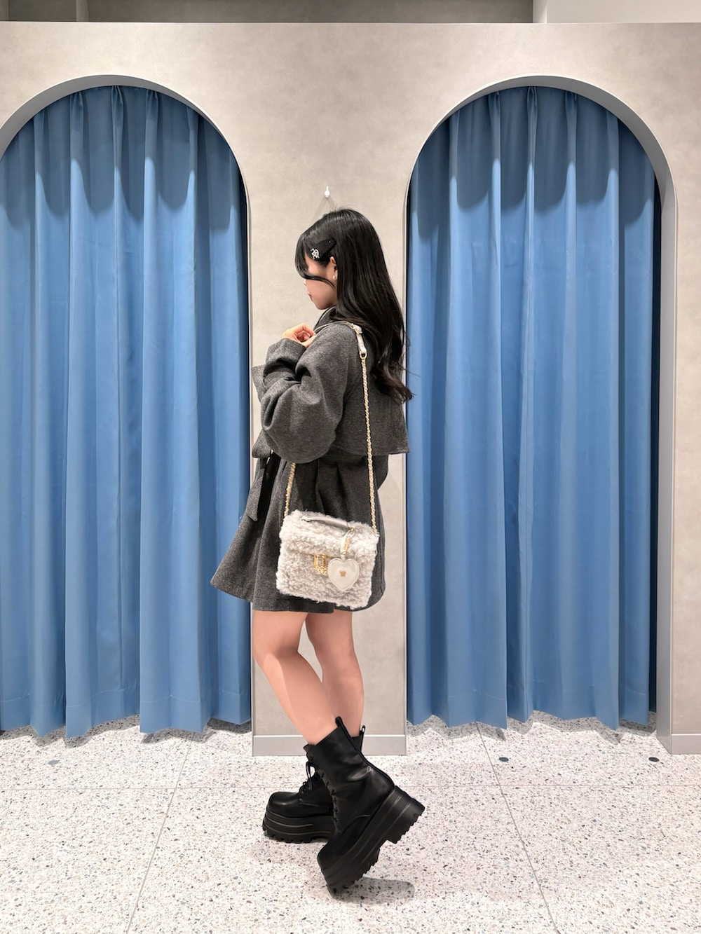 グレー系のステンカラーコート、グレー系のショルダーバッグ、ブラック系のブーツを着用したレディースの冬コーディネートの2枚目の写真