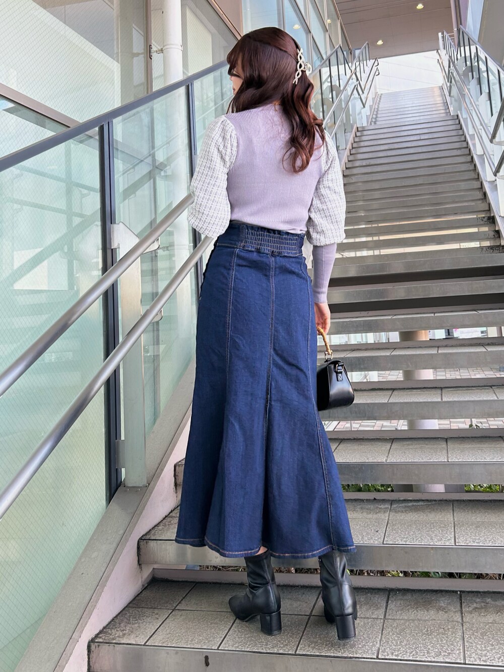 パープル系のニット/セーター、ブラック系のショルダーバッグ、ブルー系のデニムスカートを着用したレディースの冬コーディネートの2枚目の写真