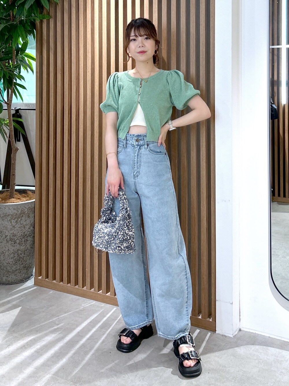 グリーン系のカーディガン/ボレロ、ホワイト系のキャミソール、ブルー系のデニムパンツを着用したレディースの春コーディネートの2枚目の写真