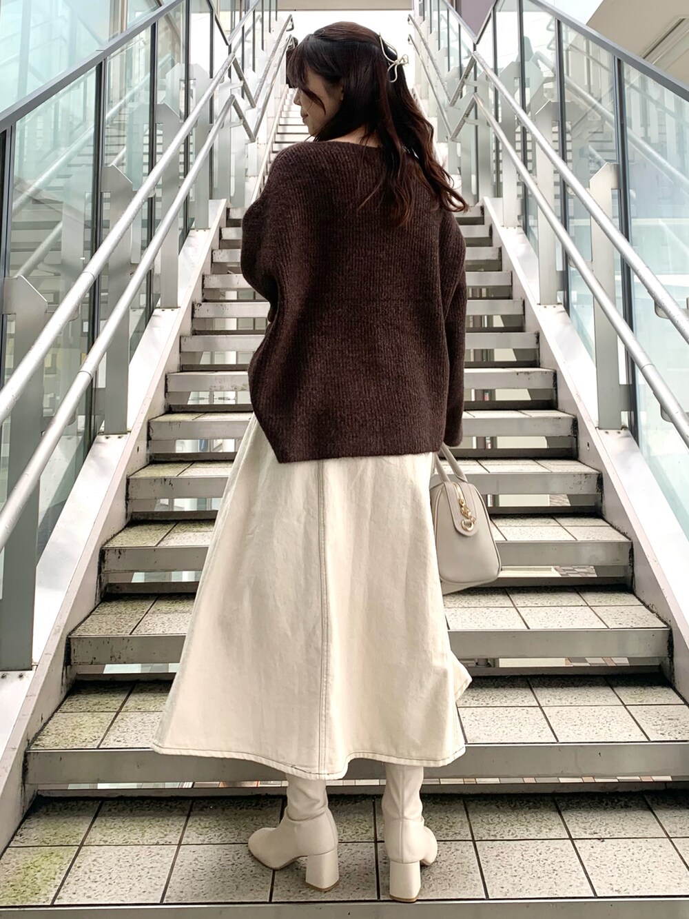 ブラウン系のニット/セーター、グレー系のボストンバッグ、ホワイト系のデニムスカートを着用したレディースの秋コーディネートの2枚目の写真