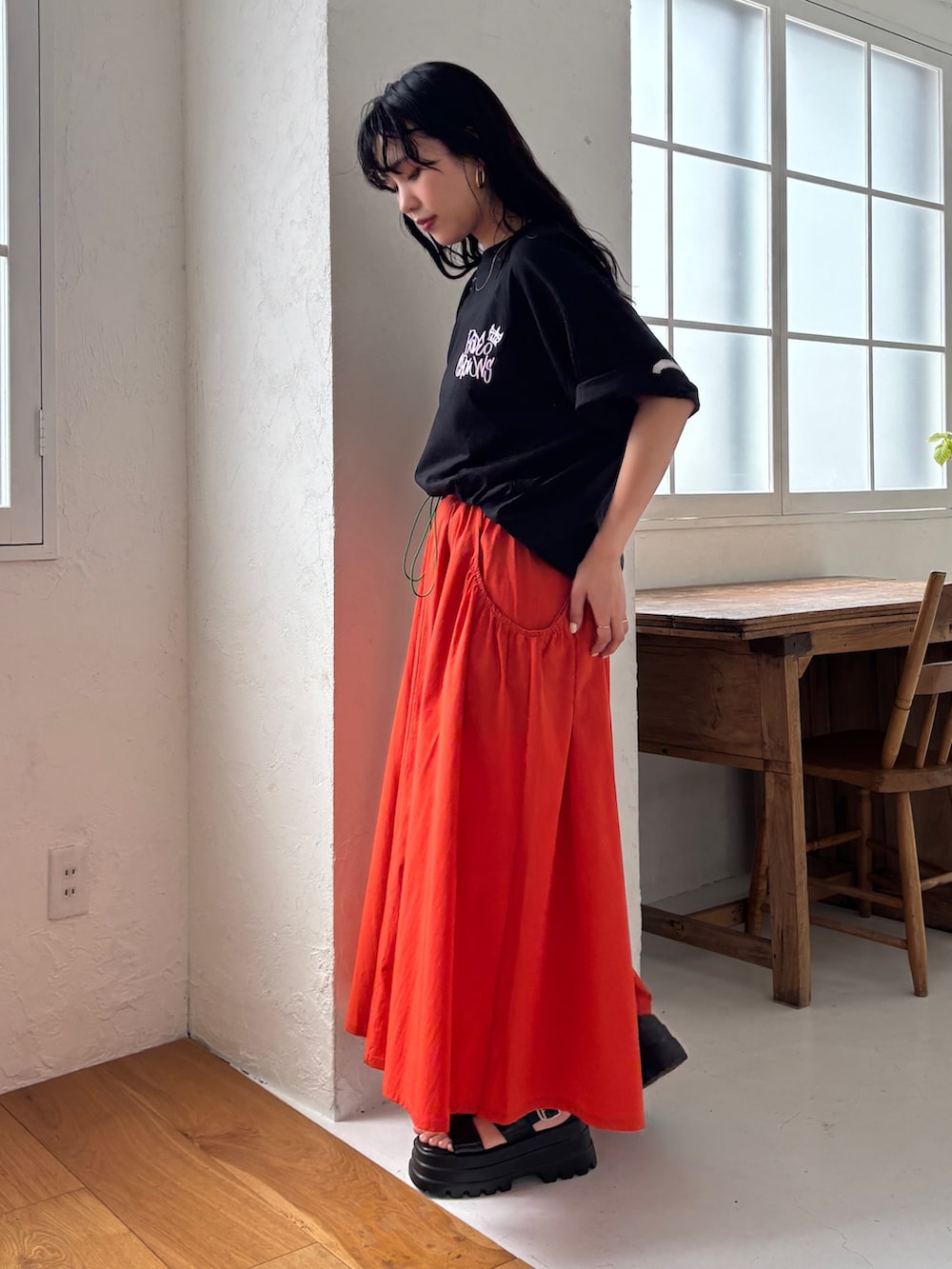 ブラック系のTシャツ/カットソー、オレンジ系のスカート、ブラック系のサンダルを着用したレディースの春コーディネートの4枚目の写真