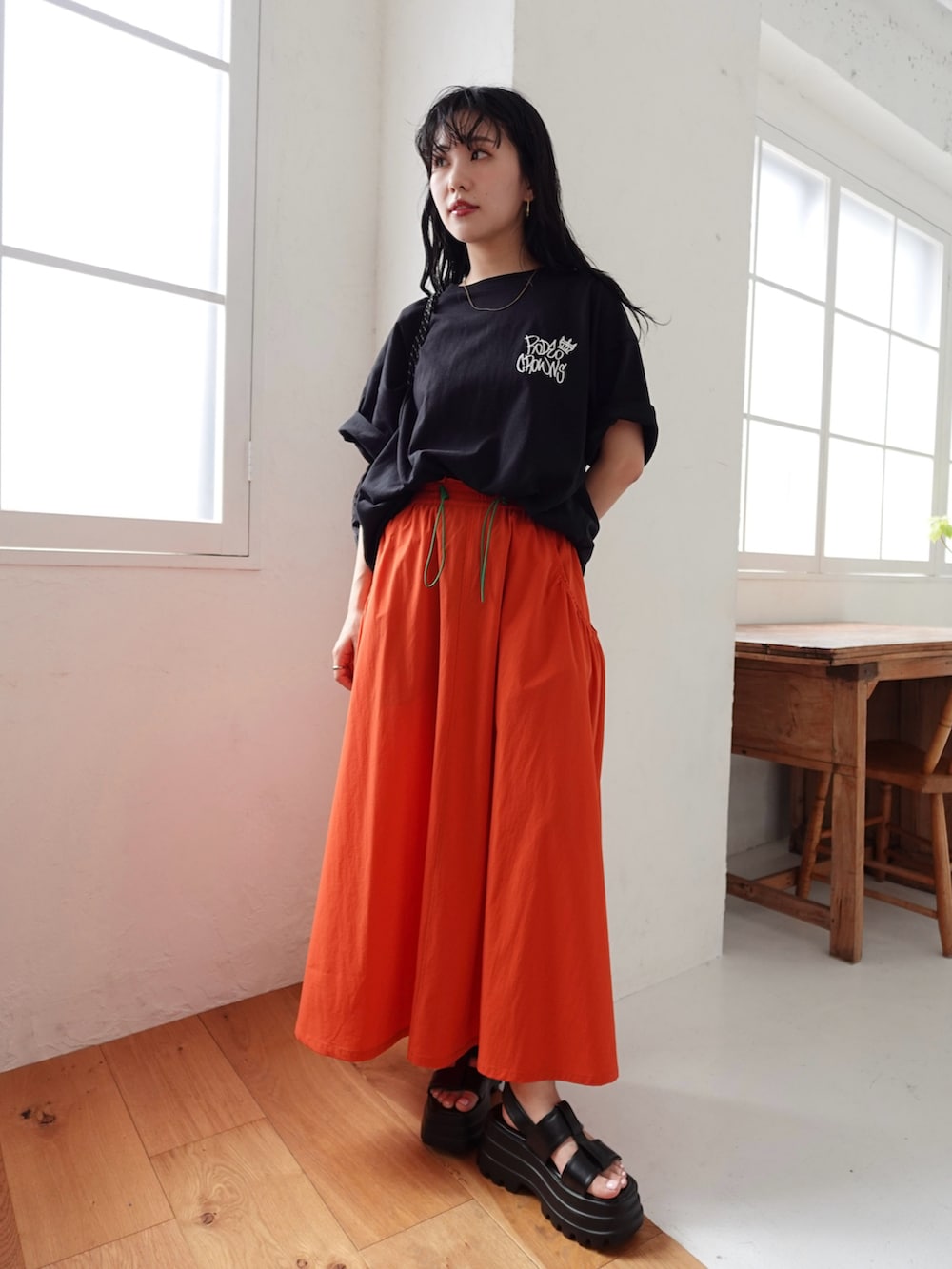 ブラック系のTシャツ/カットソー、オレンジ系のスカート、ブラック系のサンダルを着用したレディースの春コーディネートの3枚目の写真