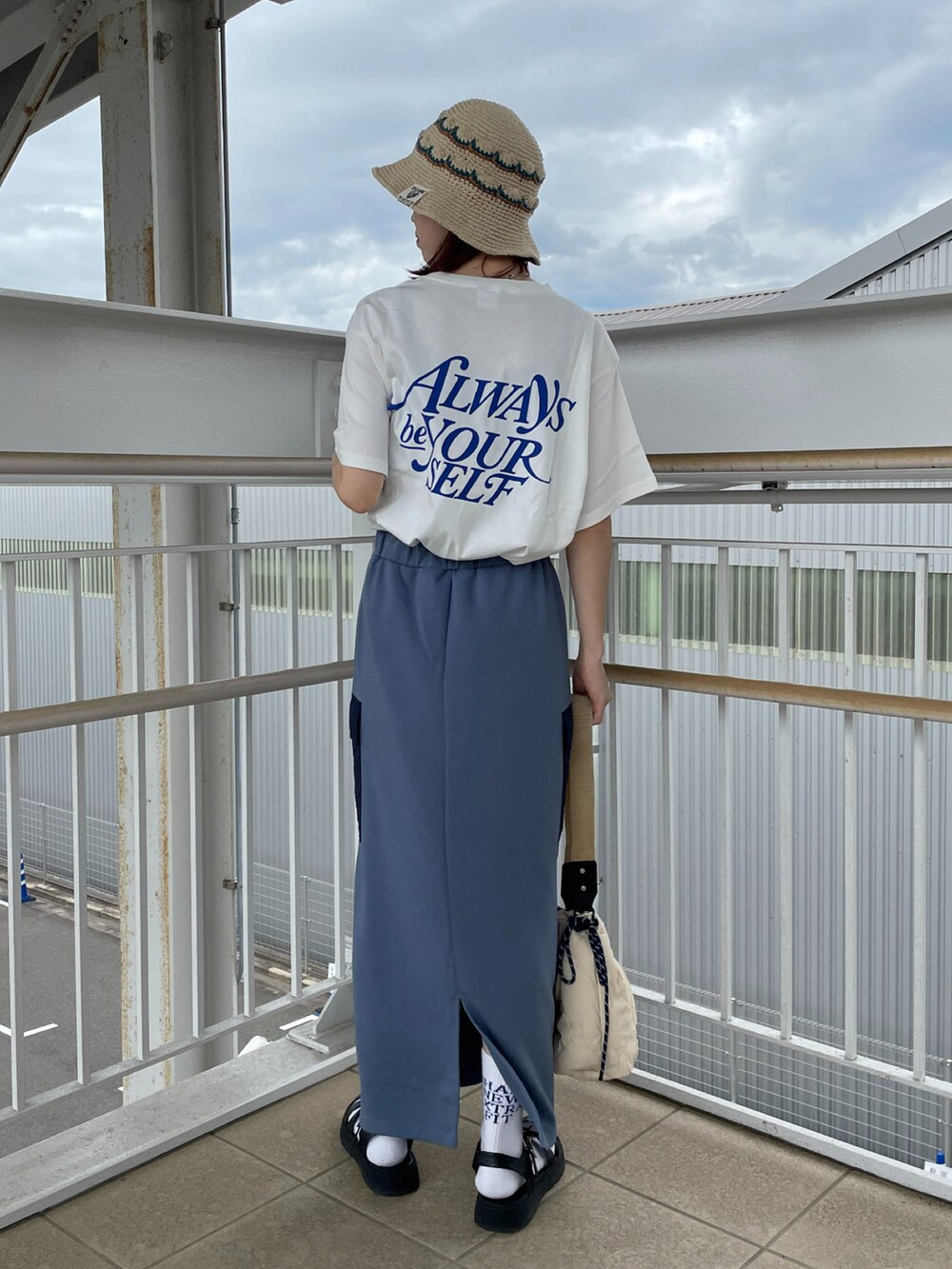 ブルー系のスカート、ホワイト系のハンドバッグ、ベージュ系のハットを着用したレディースの夏コーディネートの2枚目の写真