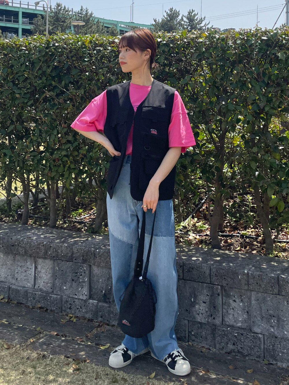 ブラック系のベスト、ブラック系のハンドバッグ、ブルー系のデニムパンツを着用したレディースの春コーディネートの2枚目の写真