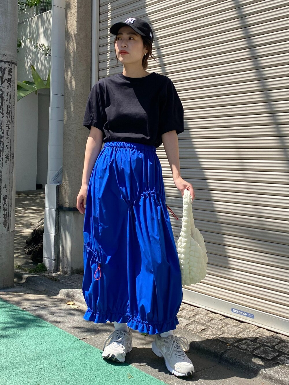 ブルー系のスカート、ブラック系のキャップを着用したレディースの春コーディネートの2枚目の写真