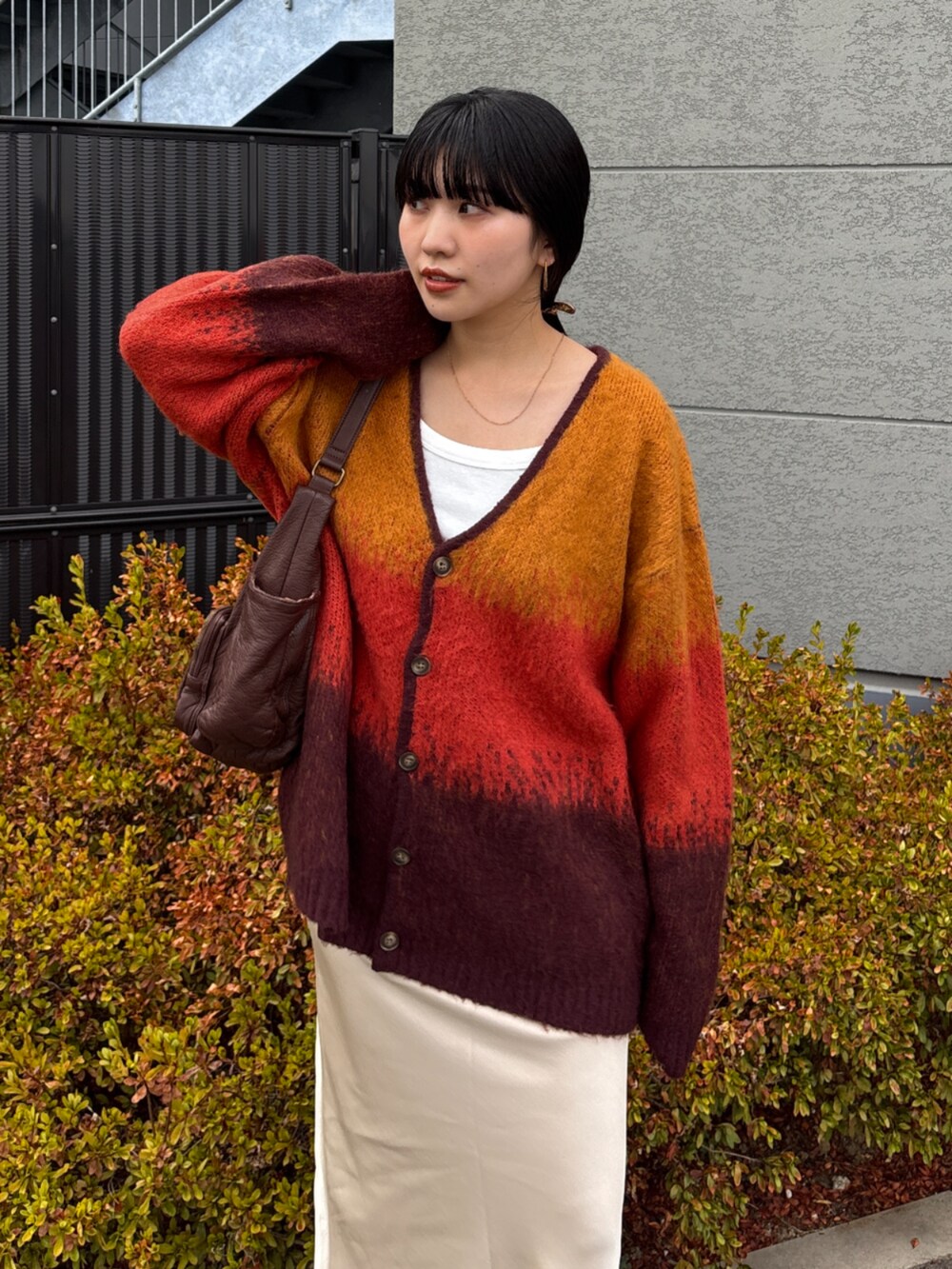 オレンジ系のカーディガン/ボレロ、ホワイト系のスカート、ブラウン系のハンドバッグを着用したレディースの秋コーディネートの2枚目の写真