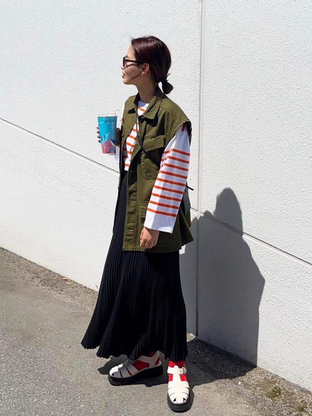 グリーン系のベスト、オレンジ系のTシャツ/カットソー、ホワイト系のサンダルを着用したレディースの春コーディネートの2枚目の写真