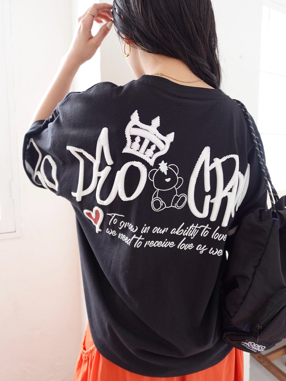 ブラック系のTシャツ/カットソー、オレンジ系のスカート、ブラック系のサンダルを着用したレディースの春コーディネートの2枚目の写真