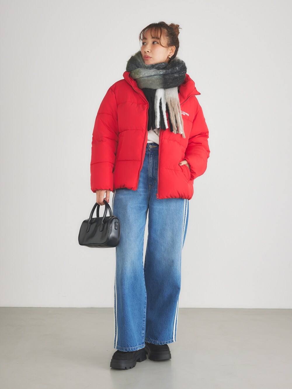 レッド系のブルゾン、ブルー系のデニムパンツ、ブラック系のマフラーを着用したレディースの冬コーディネートの2枚目の写真