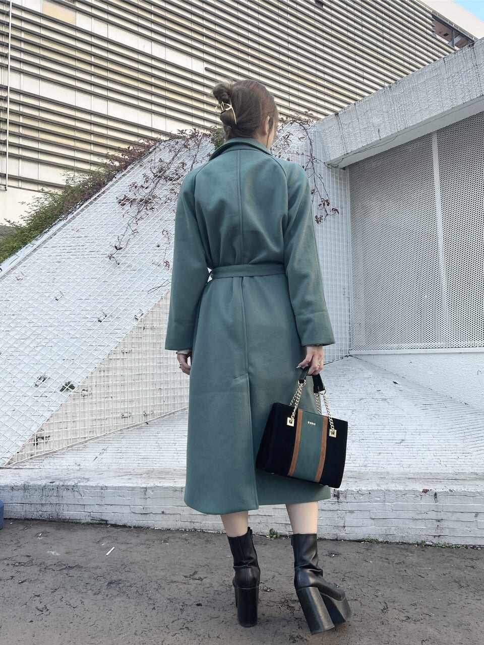 ブラック系のショルダーバッグ、グリーン系のチェスターコート、ホワイト系のTシャツ/カットソーを着用したレディースの冬コーディネートの2枚目の写真