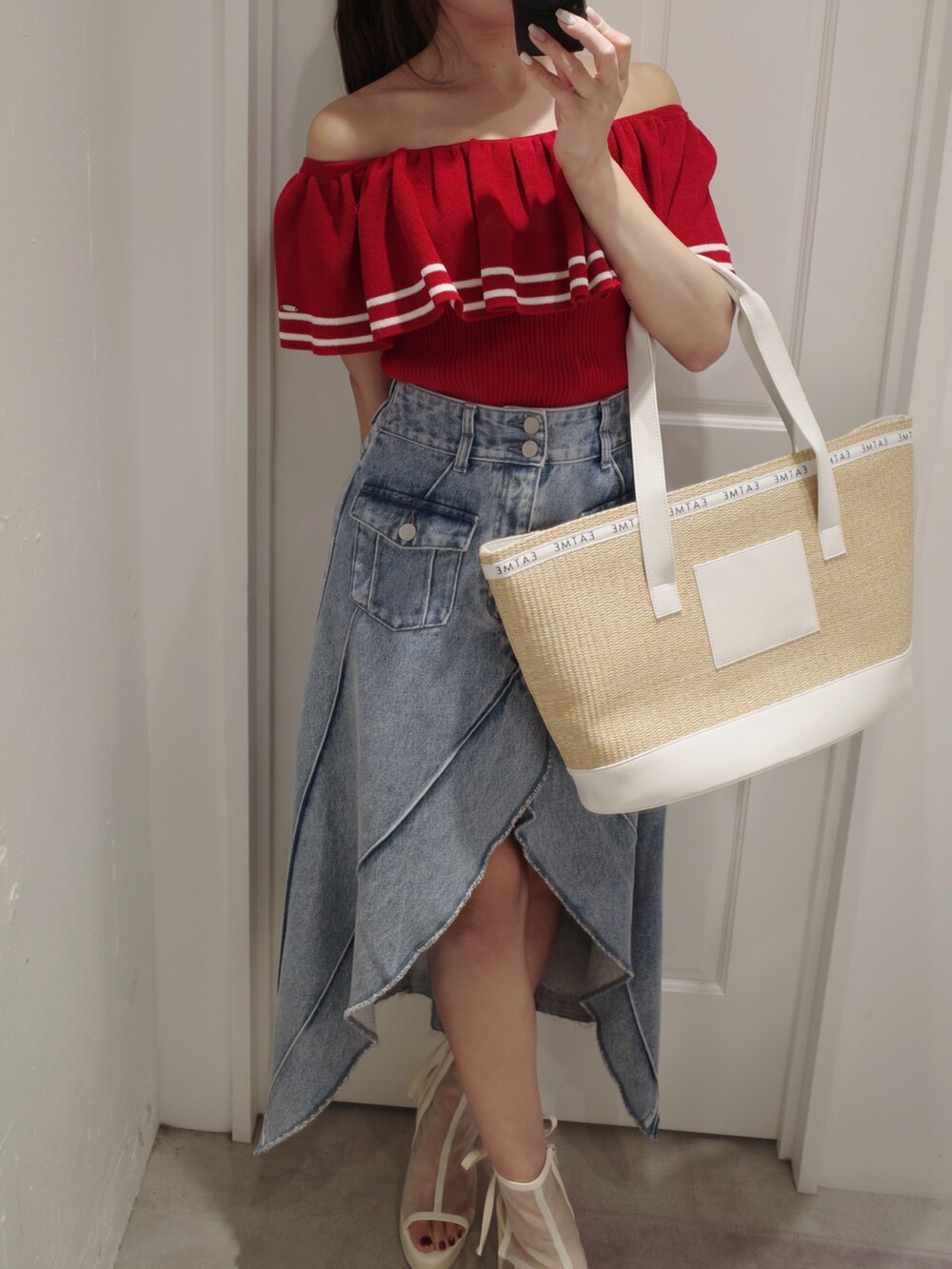 レッド系のニット/セーター、ホワイト系のトートバッグ、ブルー系のデニムスカートを着用したレディースの夏コーディネートの2枚目の写真