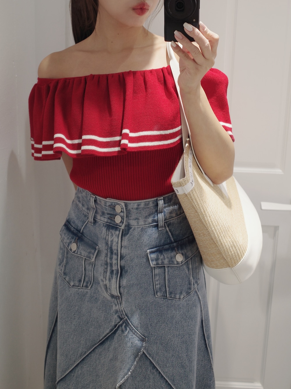 レッド系のニット/セーター、ホワイト系のトートバッグ、ブルー系のデニムスカートを着用したレディースの夏コーディネートの3枚目の写真