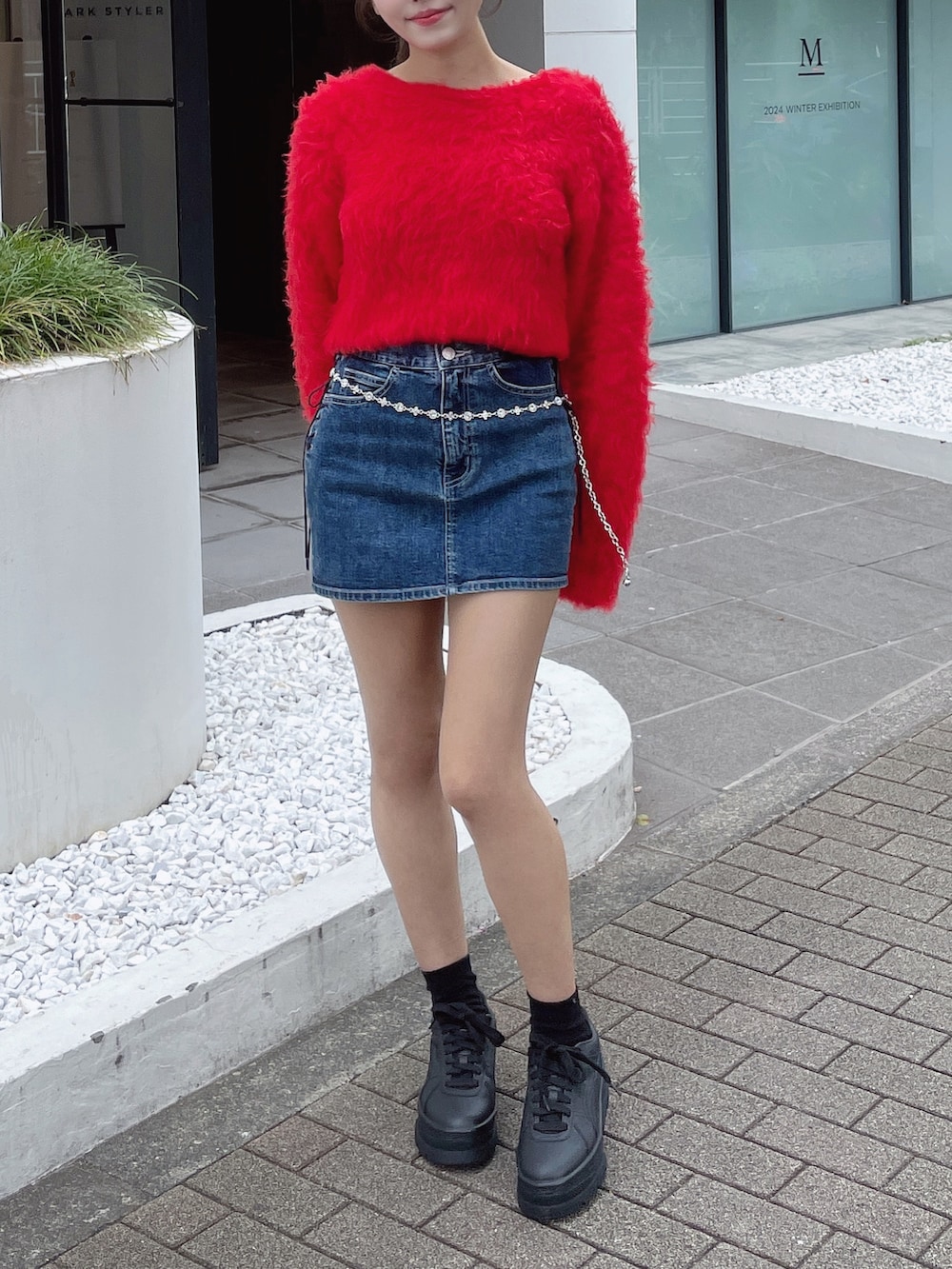 レッド系のニット/セーター、ホワイト系のスニーカー、ブルー系のデニムスカートを着用したレディースの秋コーディネートの4枚目の写真