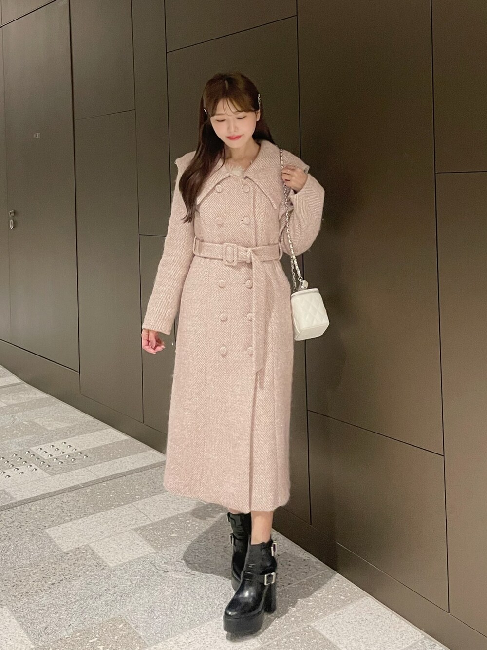 ホワイト系のハンドバッグ、ピンク系のチェスターコート、ブラック系のブーツを着用したレディースの冬コーディネートの2枚目の写真