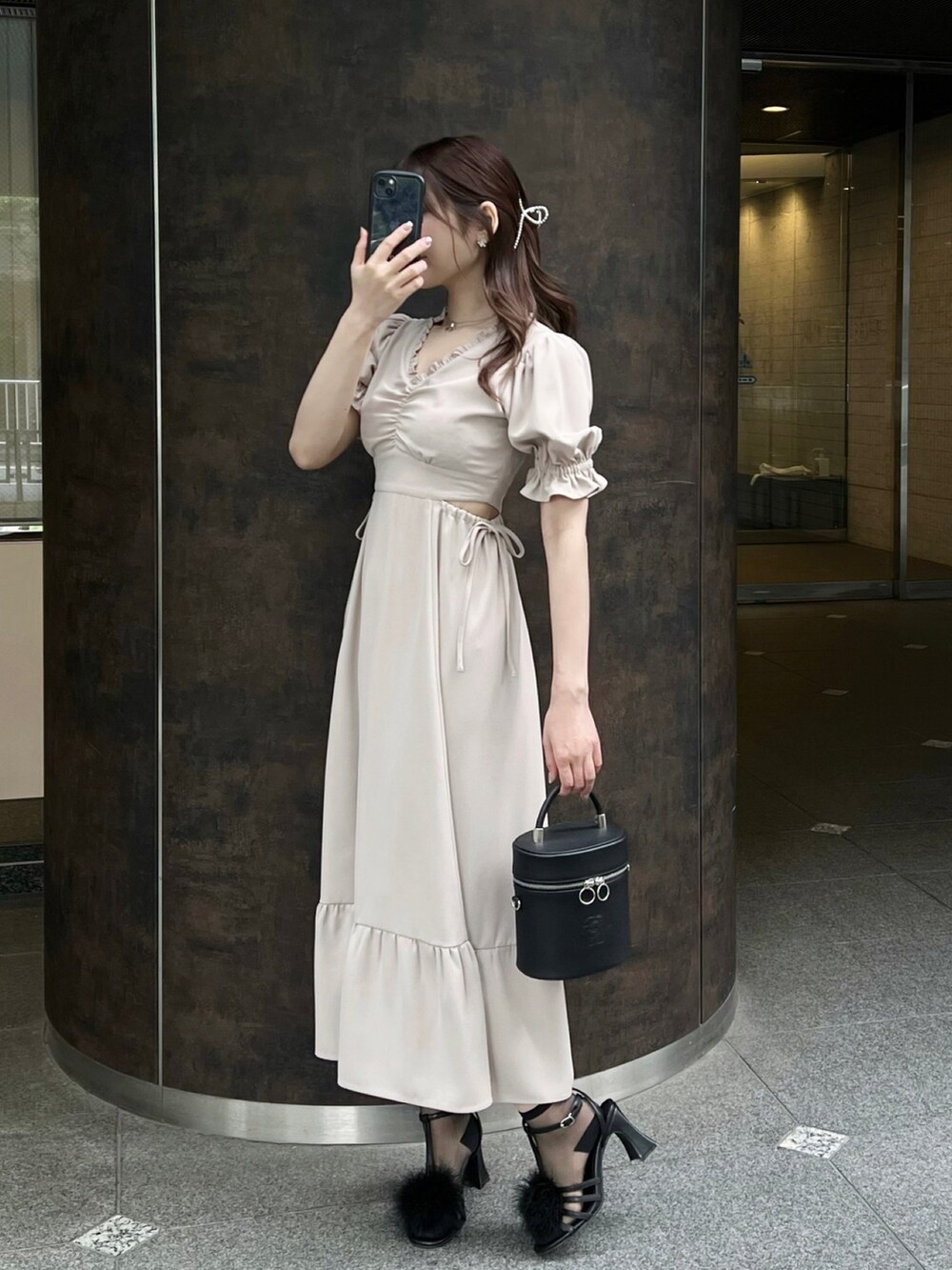 ブラック系のハンドバッグ、ベージュ系のワンピース、ブラック系のサンダルを着用したレディースの春コーディネートの3枚目の写真