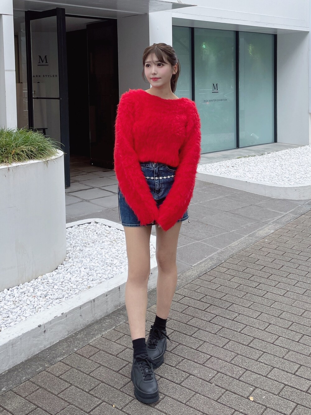 レッド系のニット/セーター、ホワイト系のスニーカー、ブルー系のデニムスカートを着用したレディースの秋コーディネートの2枚目の写真