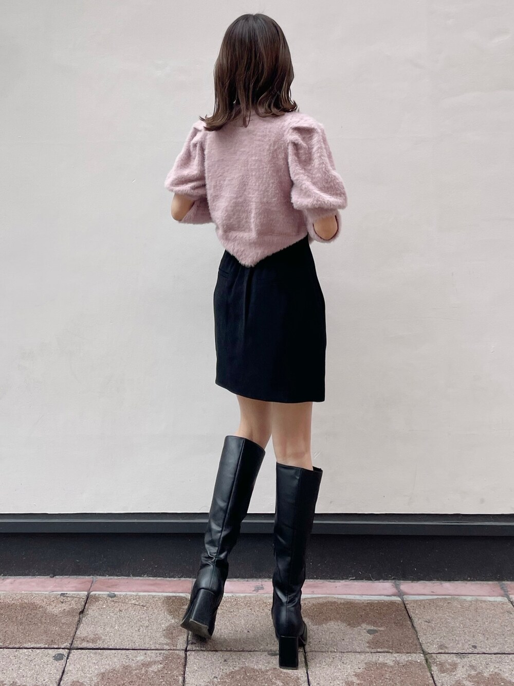 ピンク系のニット/セーター、ブラック系のスカート、ブラック系のブーツを着用したレディースの冬コーディネートの2枚目の写真