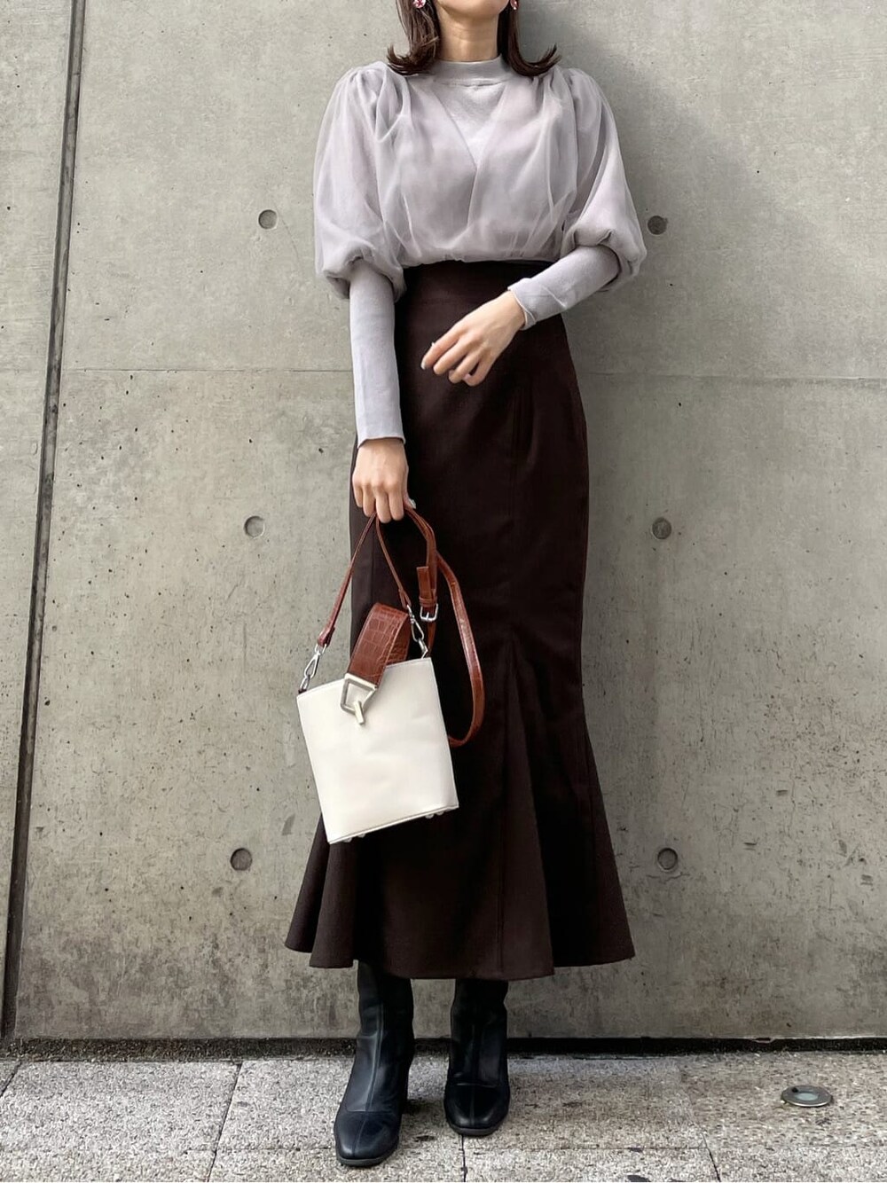 グレー系のニット/セーター、ブラック系のブーツ、ブラウン系のスカートを着用したレディースの秋コーディネートの2枚目の写真