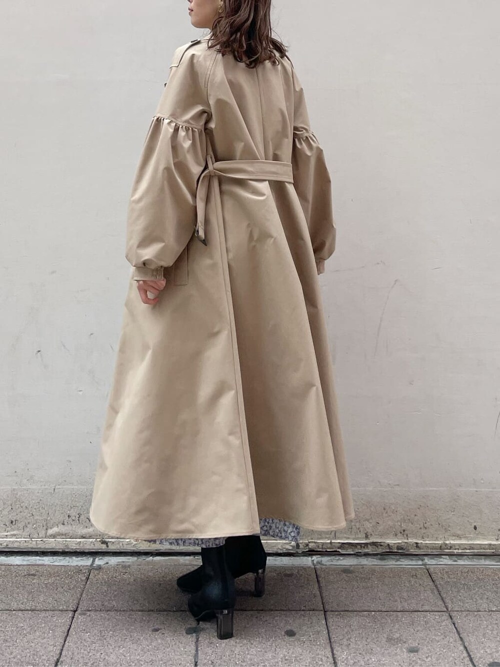 ベージュ系のトレンチコート、ブルー系のワンピース、ブラック系のブーツを着用したレディースの冬コーディネートの4枚目の写真