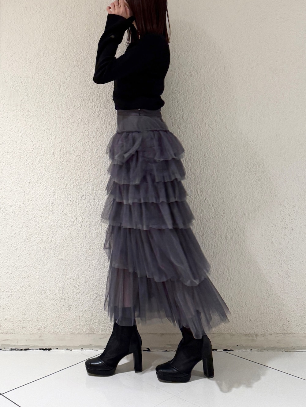 グレー系のスカート、ブラック系のニット/セーター、ブラック系のブーツを着用したレディースの春コーディネートの3枚目の写真