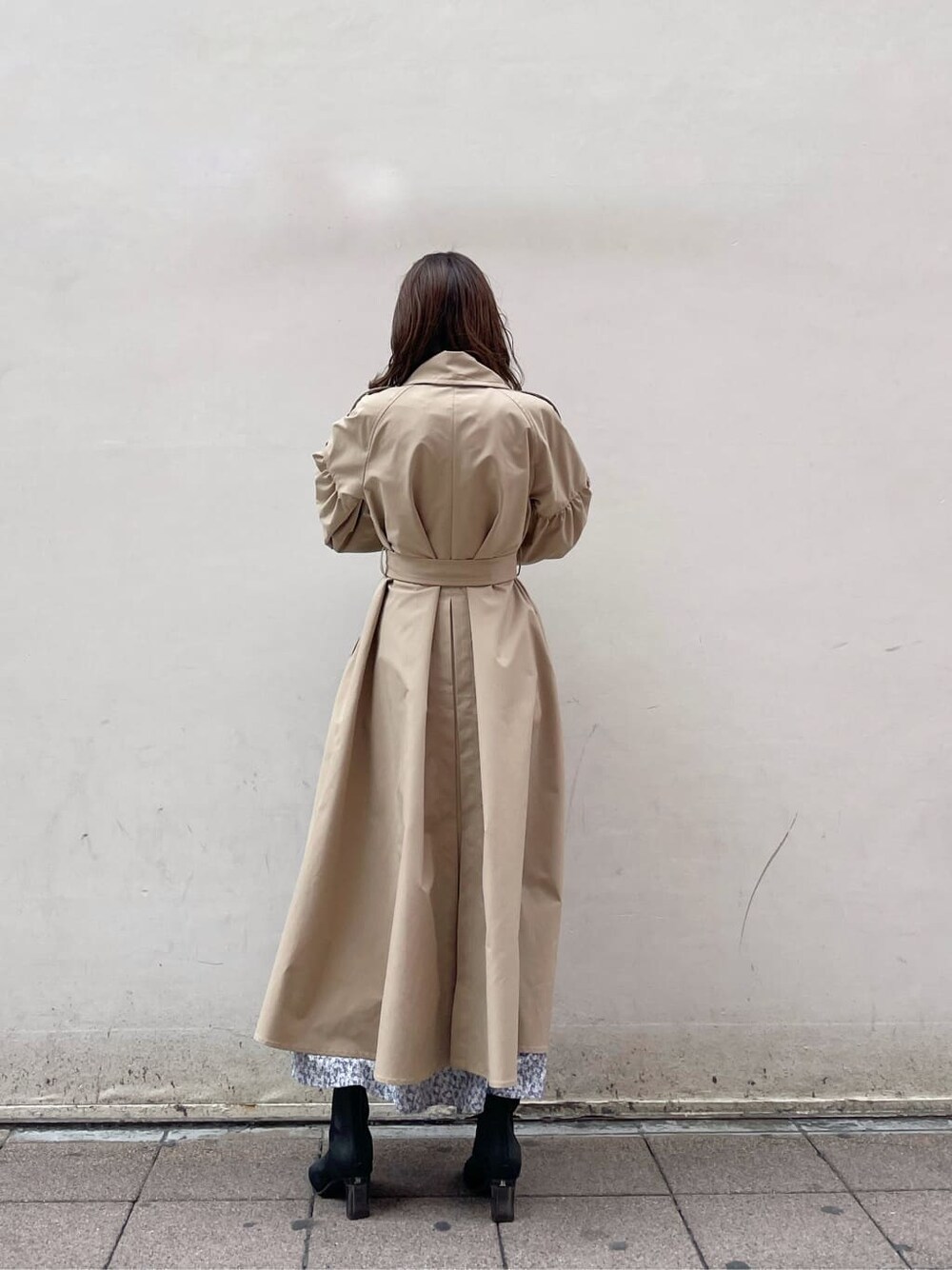 ベージュ系のトレンチコート、ブルー系のワンピース、ブラック系のブーツを着用したレディースの冬コーディネートの2枚目の写真