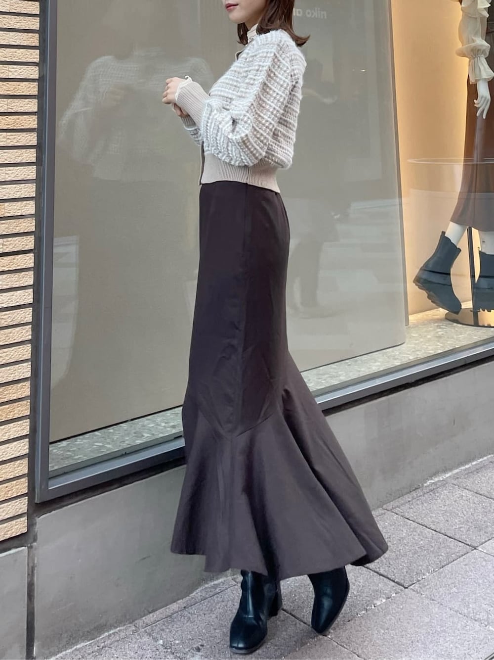 ブラウン系のスカート、ブラック系のブーツ、ベージュ系のカーディガン/ボレロを着用したレディースの秋コーディネートの2枚目の写真