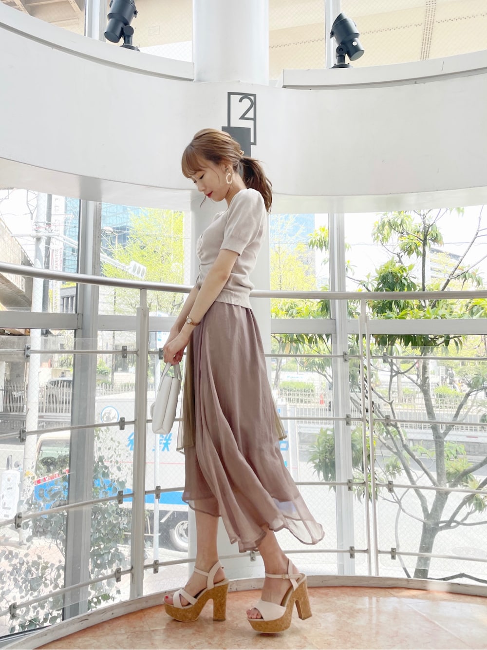 ブラウン系のスカート、ベージュ系のサンダル、ホワイト系のハンドバッグを着用したレディースの春コーディネートの2枚目の写真