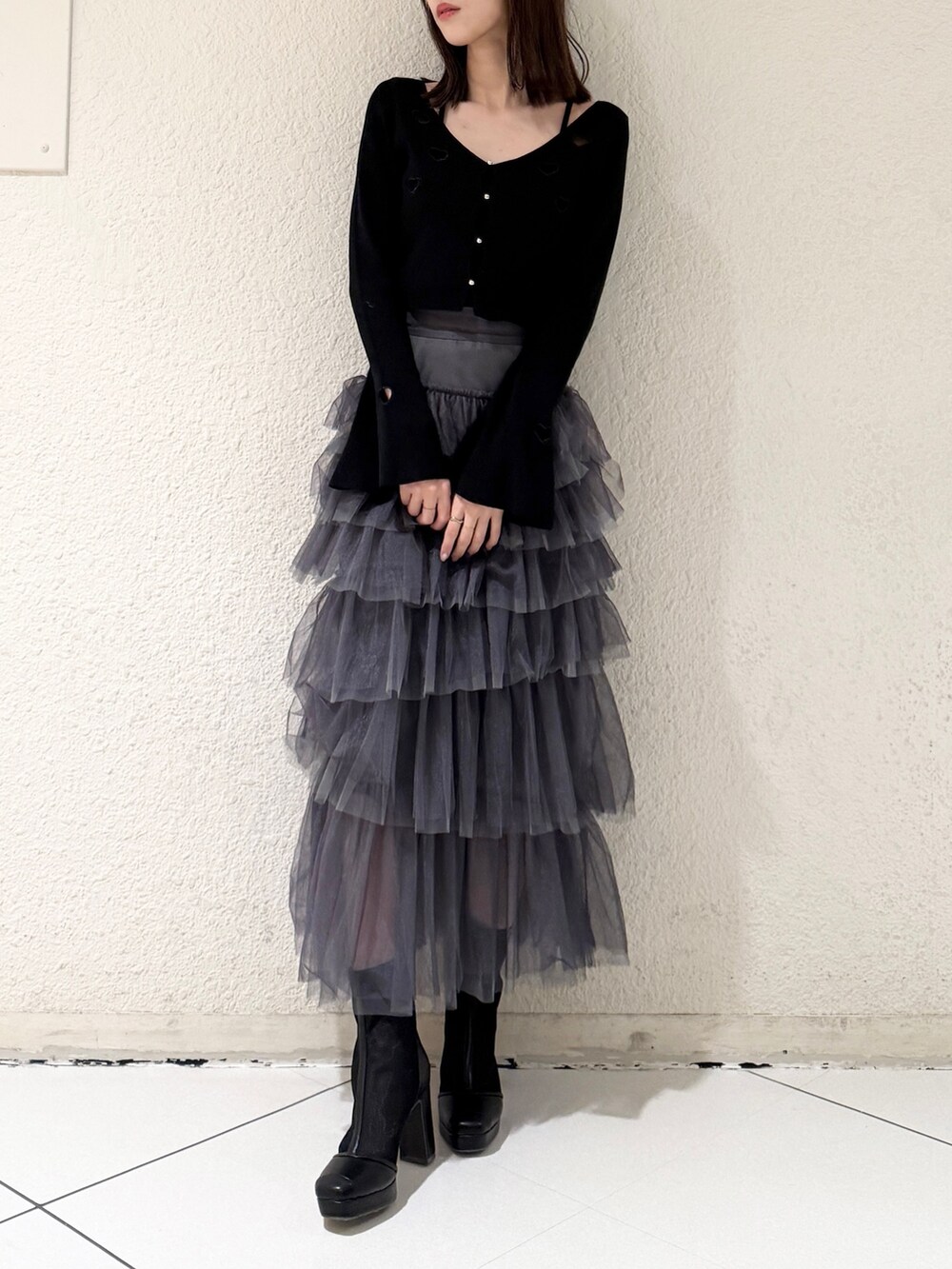 グレー系のスカート、ブラック系のニット/セーター、ブラック系のブーツを着用したレディースの春コーディネートの2枚目の写真