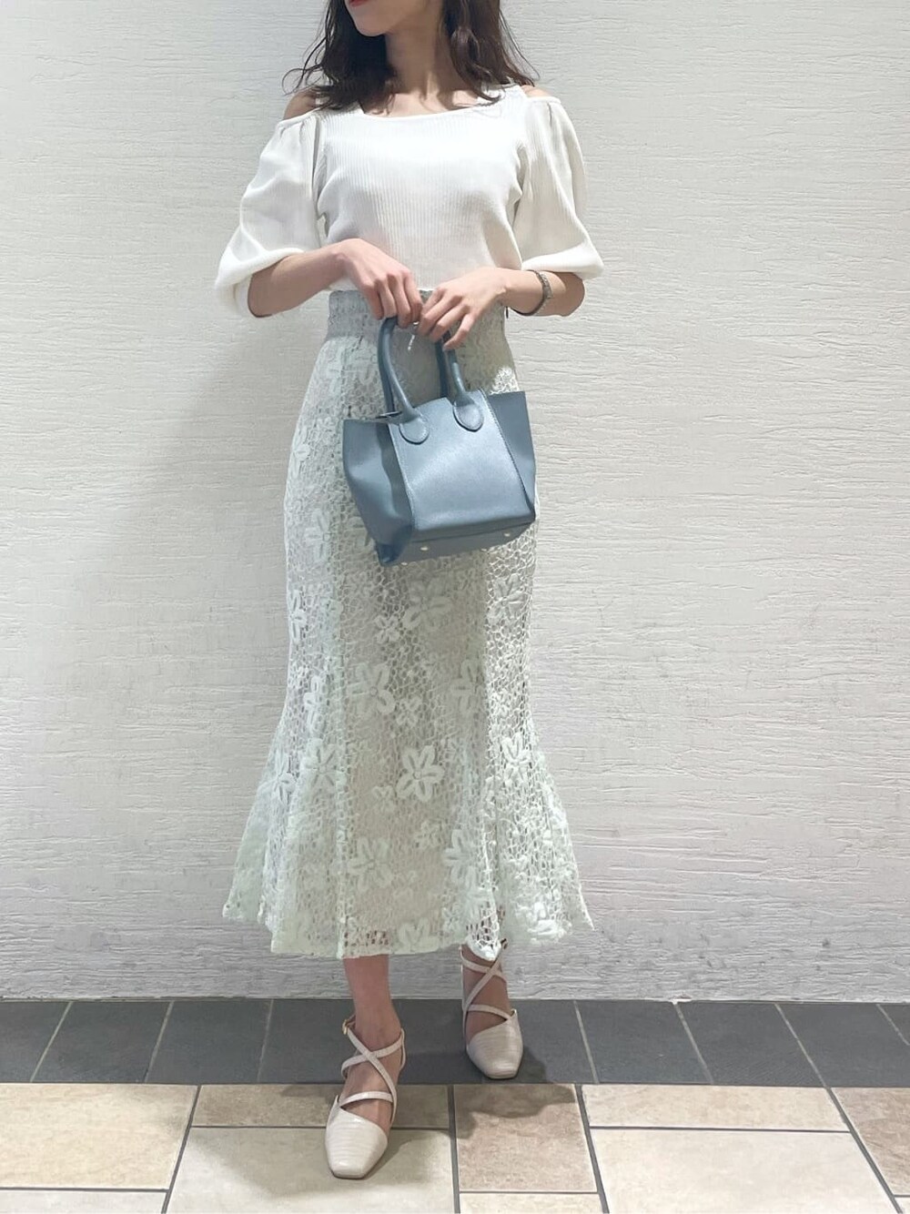 ホワイト系のニット/セーター、ブルー系のスカート、ブルー系のハンドバッグを着用したレディースの春コーディネートの2枚目の写真