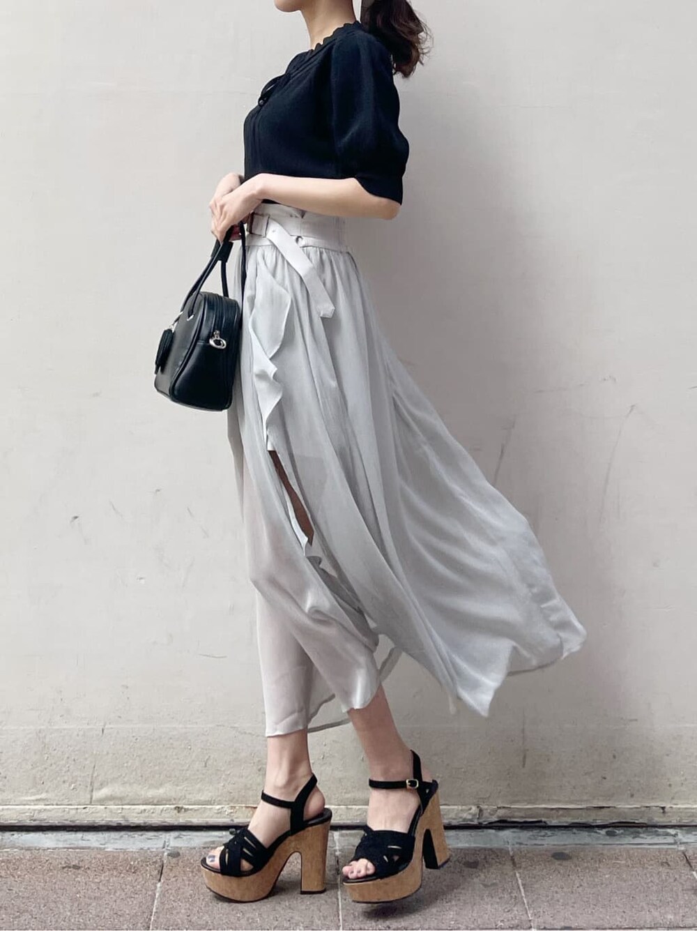 グレー系のスカート、ブラック系のサンダル、ホワイト系のニット/セーターを着用したレディースの春コーディネートの2枚目の写真