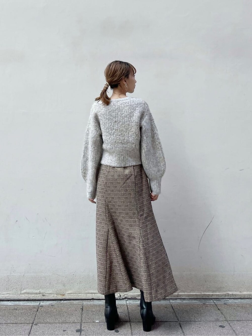 ブラック系のブーツ、ベージュ系のニット/セーター、ゴールド系のスカートを着用したレディースの秋コーディネートの3枚目の写真