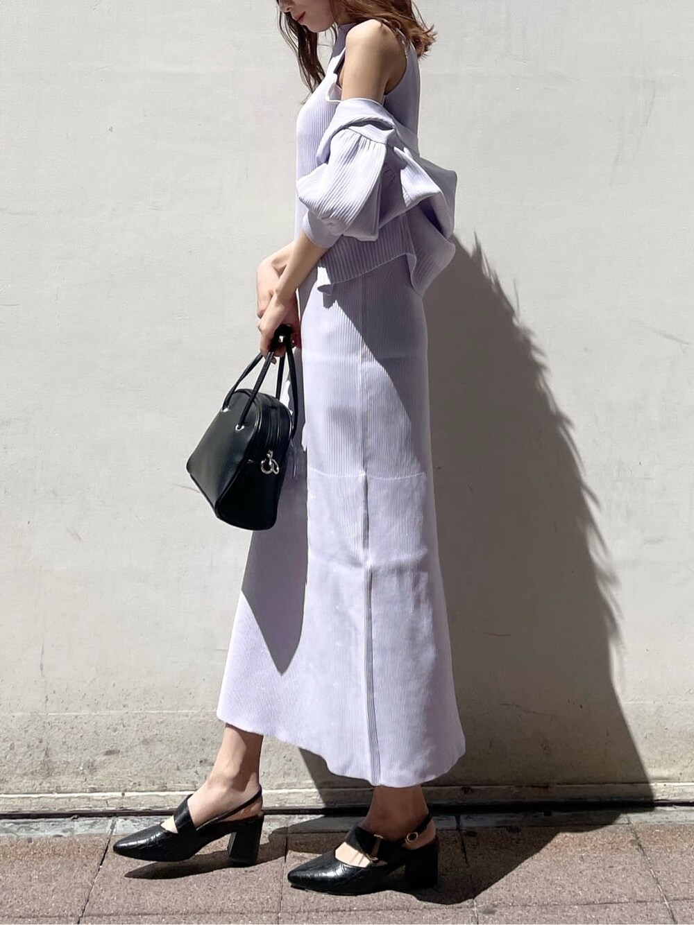 パープル系のワンピース、ブラック系のパンプス、ブラック系のハンドバッグを着用したレディースの春コーディネートの2枚目の写真