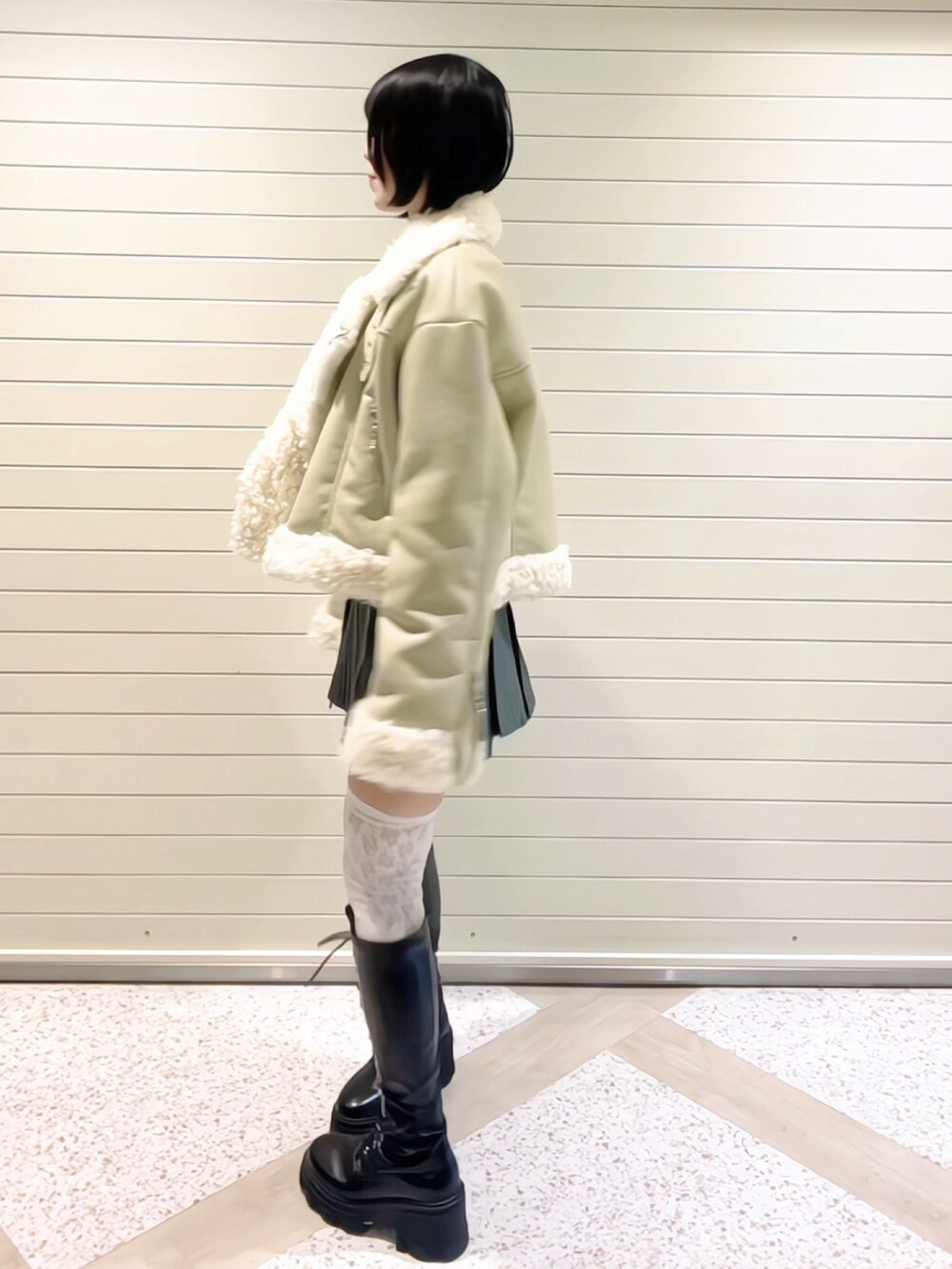 ホワイト系のムートンコート、グレー系のスカート、ブラック系のブーツを着用したレディースの冬コーディネートの3枚目の写真