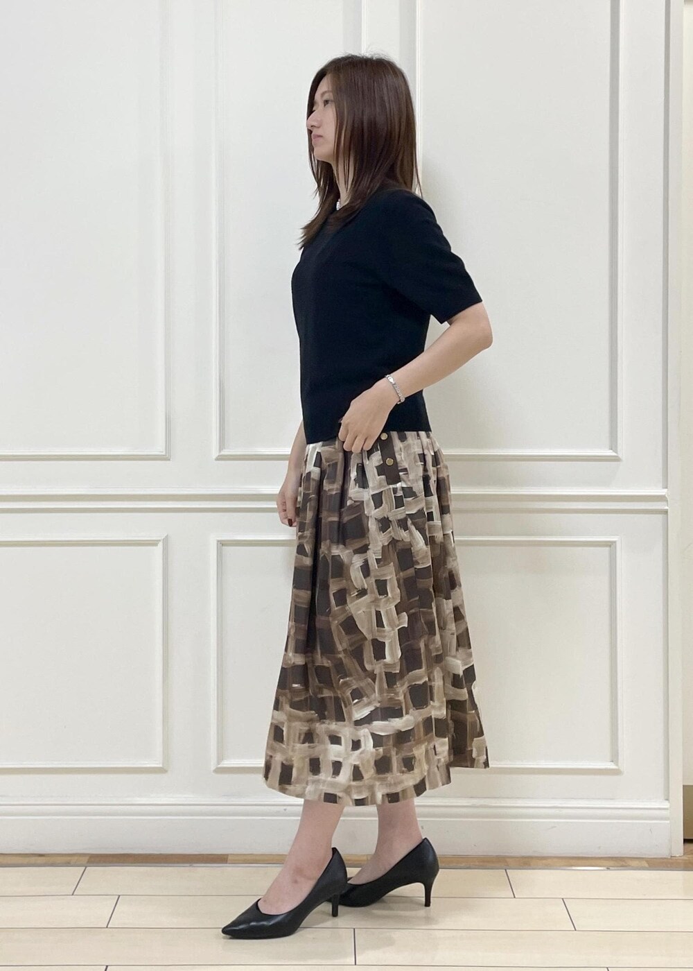 グレー系のハンドバッグ、ブラウン系のスカート、ブラック系のニット/セーターを着用したレディースの秋コーディネートの2枚目の写真