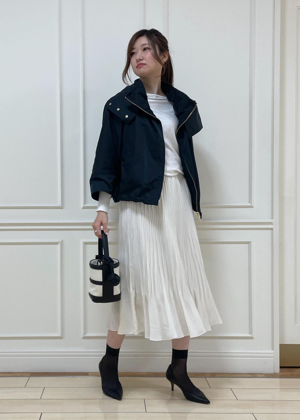 ブラック系のパンプス、ホワイト系のスカート、ブラック系のハンドバッグを着用したレディースの春コーディネートの2枚目の写真
