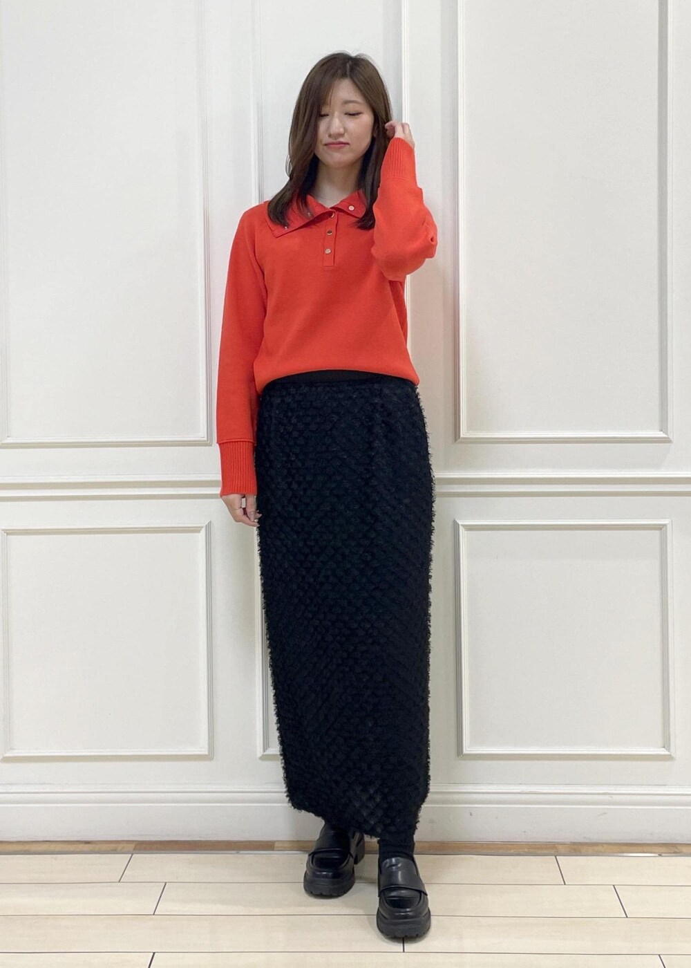 レッド系のニット/セーター、ブラック系のスカート、ベージュ系のハンドバッグを着用したレディースの秋コーディネートの2枚目の写真