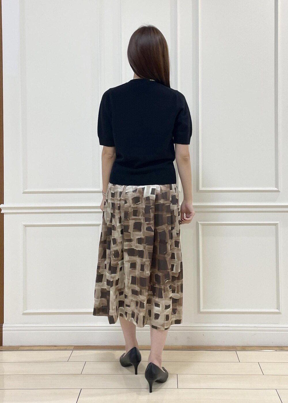 グレー系のハンドバッグ、ブラウン系のスカート、ブラック系のニット/セーターを着用したレディースの秋コーディネートの3枚目の写真